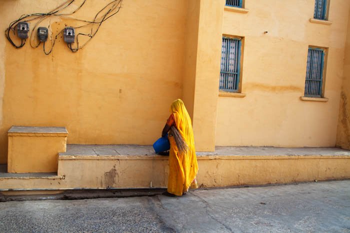 using colour in street photography composition, picture shows a woman dressed in yellow with her back to the camera, facing the yellow wall of a building