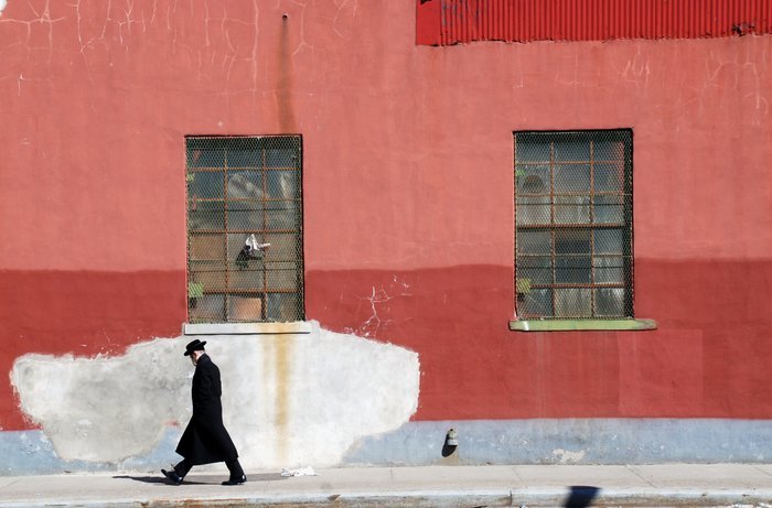 スーツと帽子をかぶった男が赤い壁を通り過ぎて歩く