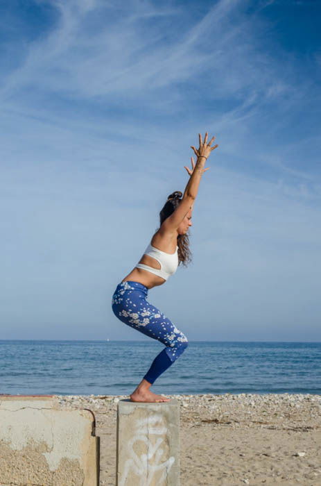 Female model balancing in chair pose with the sea in the background