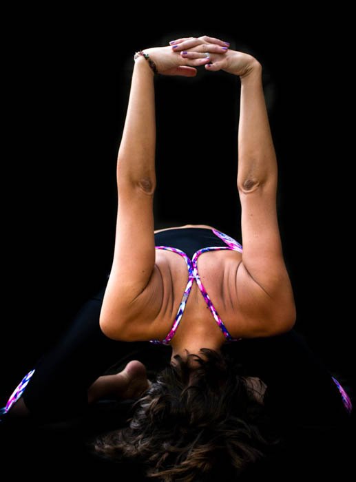 Photo of a yogini in a forward bend pose, showing creative use of black background in photography