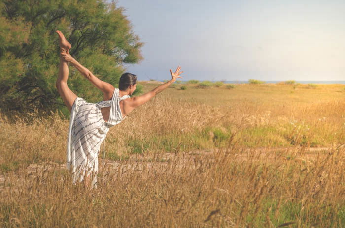 Girl wearing a white dress performing dancer's pose in a field of wheat