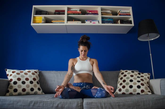 Creative yoga photography showing a female model in lotus pose on a grey couch