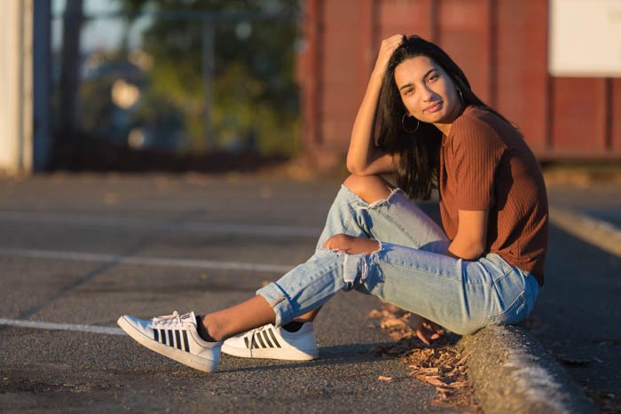 A girl posing sitting on the ground of an outdoor carpark