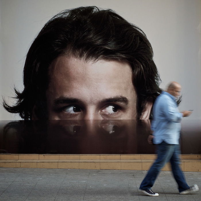  Les yeux rivés sur une publicité semblent suivre un homme marchant - photographie de rue 