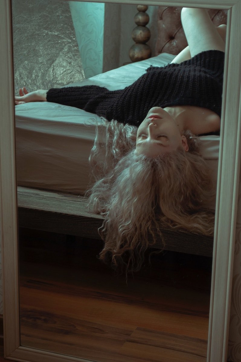 Woman lying on a bed with her head hang on the edge and her hair flowing down