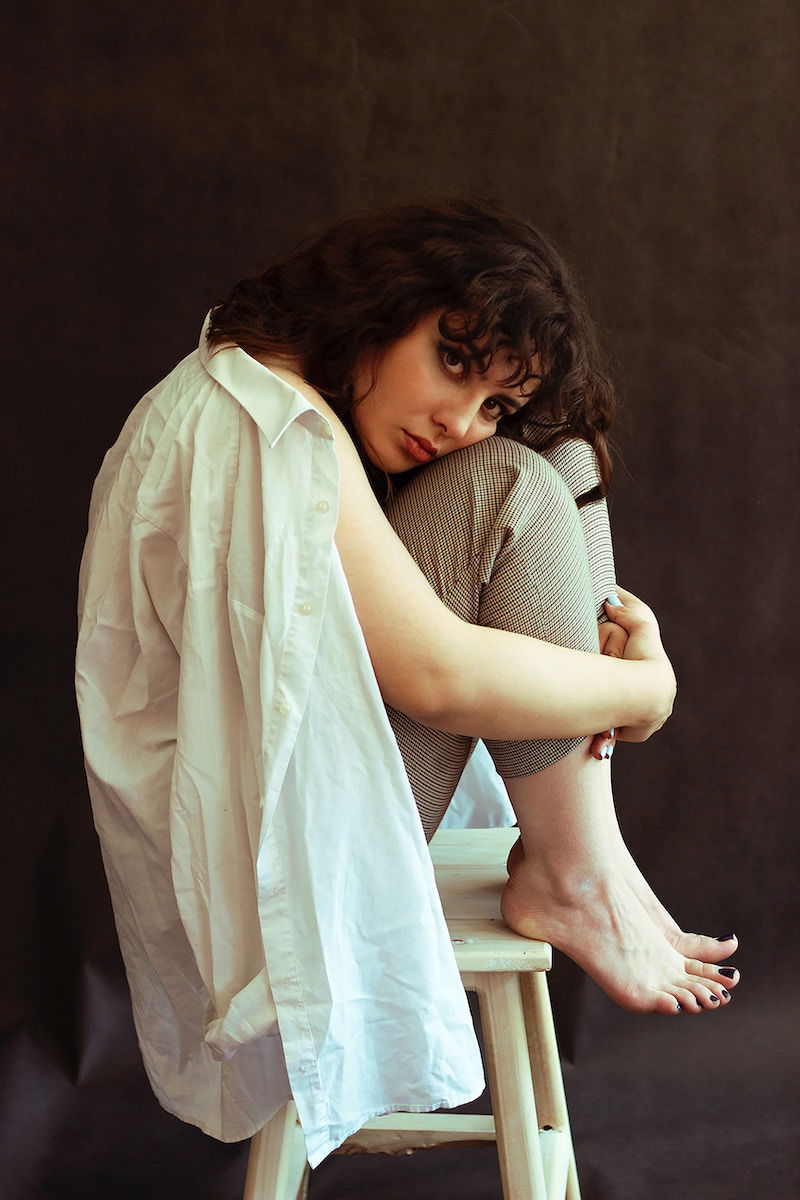 Woman posing on a stool with her knees up to her chest and her arms around her legs