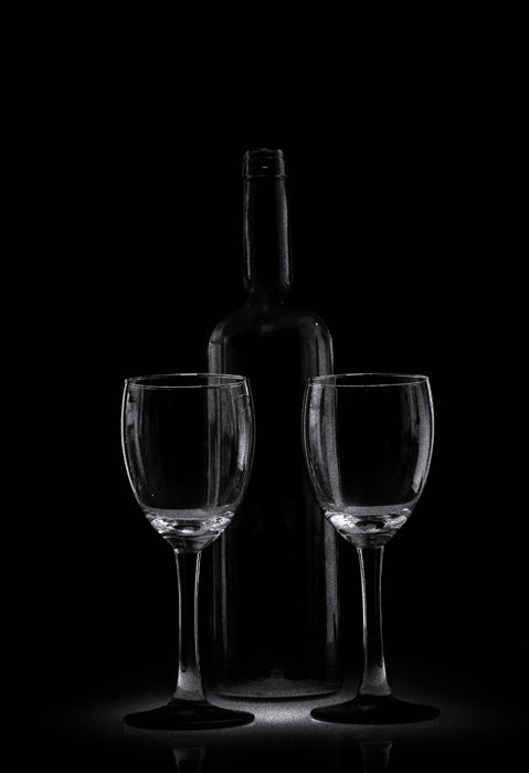 Two glasses and a glass bottle sit in a low key dark environment 