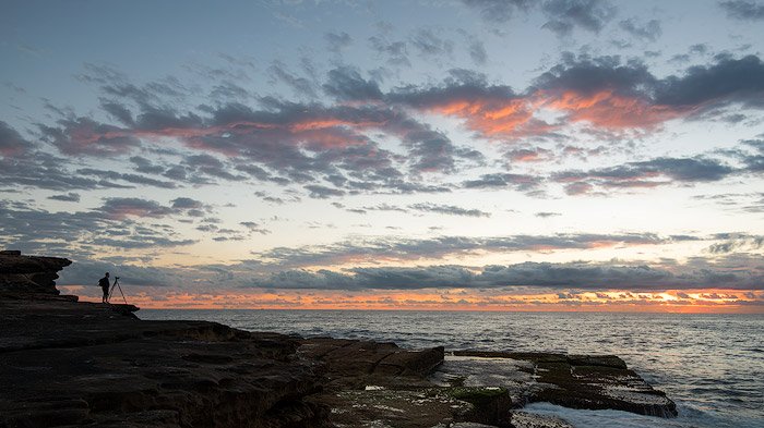 A photographer taking sunrise photography at a rocky coast