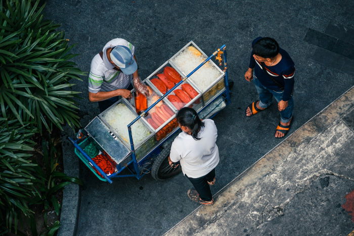 A street photography shot of a food vendor serves food from his cart 