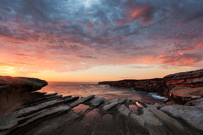 Rock reflections by a coastal seascape at sunrise