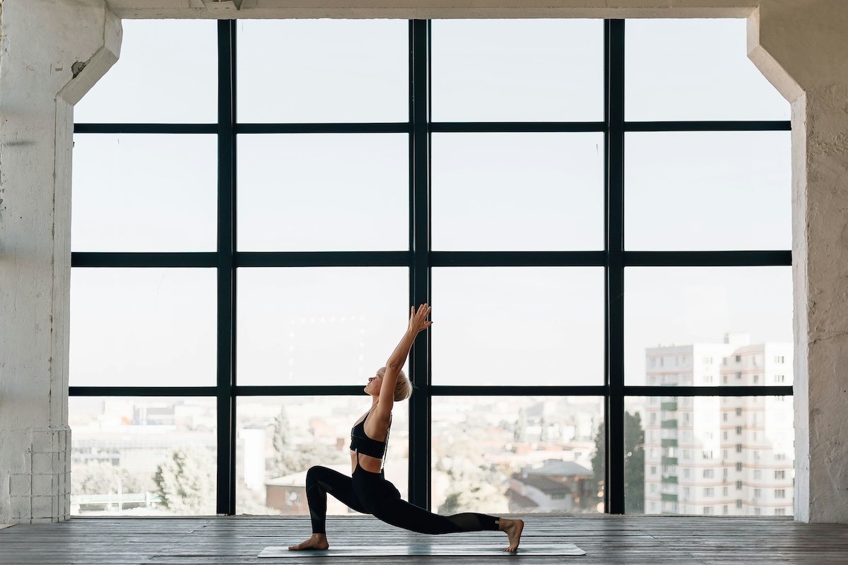 A yogini doing a low lunge in front of a large wall of windows as an example of yoga photography