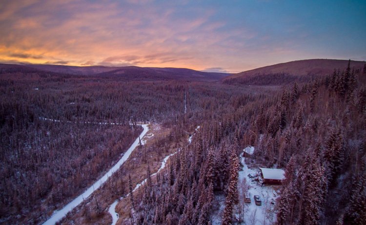 Aerial photography view of a forest, houses and mountains taken by a drone at sunset