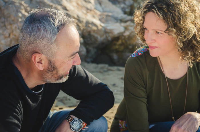 Relaxed posed photo of a couple sitting outdoors smiling at each other