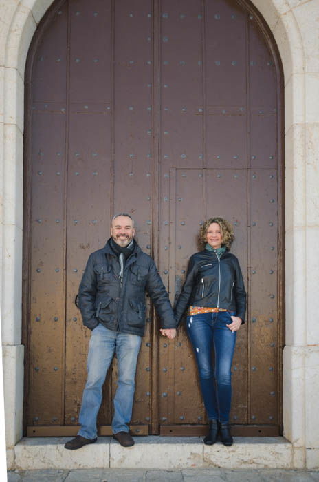 A couple poses holding hands in front of a doorway 