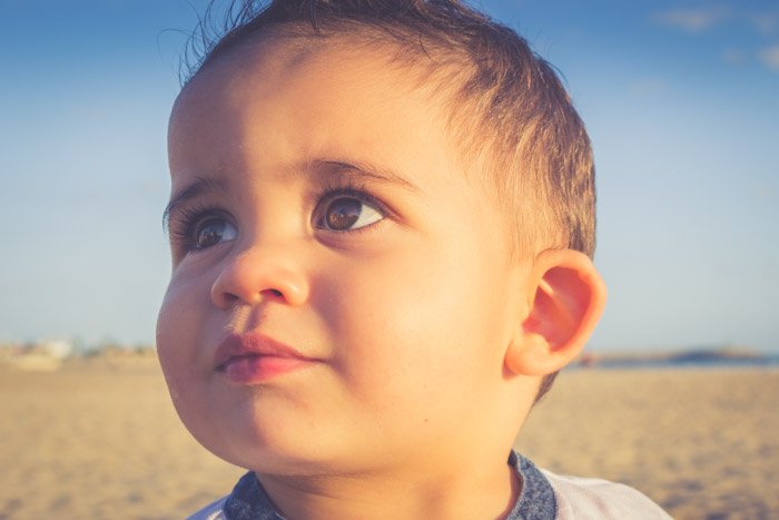 A boy looks off camera in a beach location during the golden hour
