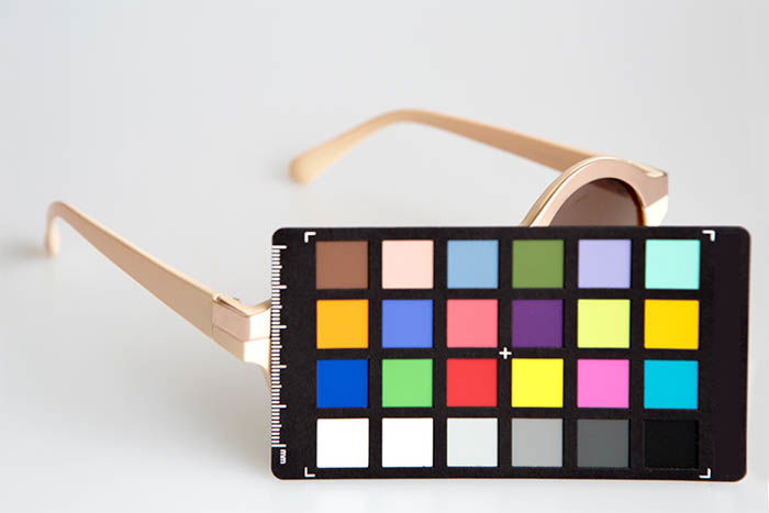 A pair of beige women's sunglasses in front of white background, and a color chart in front on them