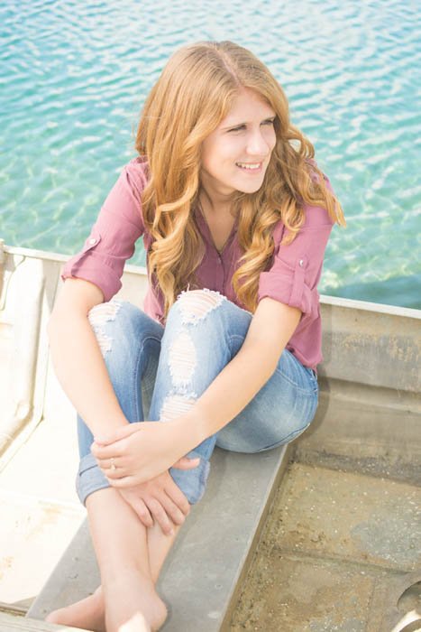 portrait of a redheaded girl sitting on a pier with light reflectors used for lighting