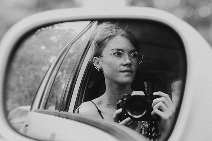 creative black and white self portrait of a young woman in the mirror of her car