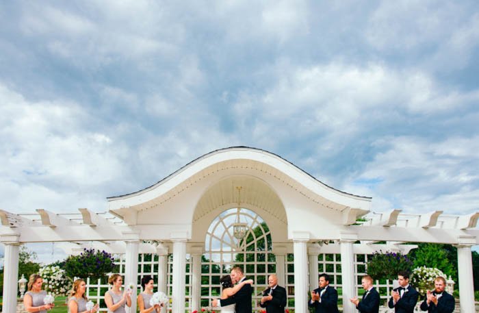 The bridal party, bridesmaids and groomsmen applauding as bride and groom kiss