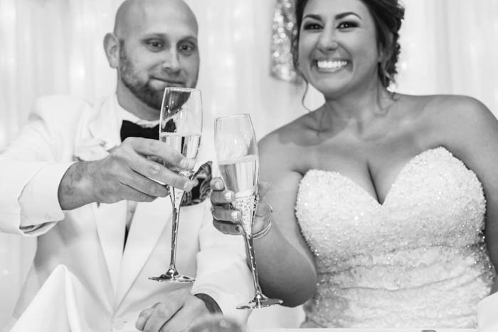 A black and white portrait of a bride and groom toasting at their wedding reception