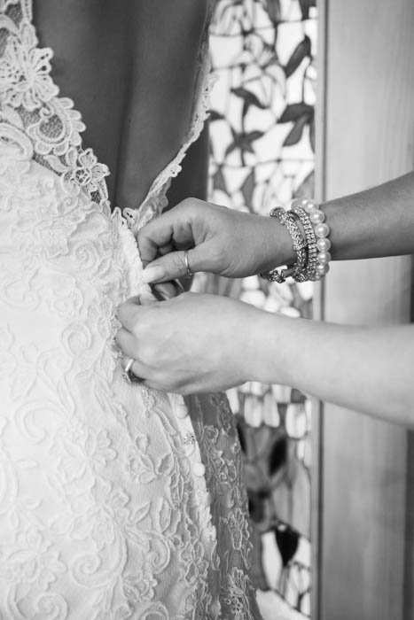 A black and white wedding photo of mother of the bride buttoning wedding dress 