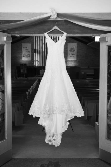 A black and white Wedding Photo of a wedding dress hanging above the church doors