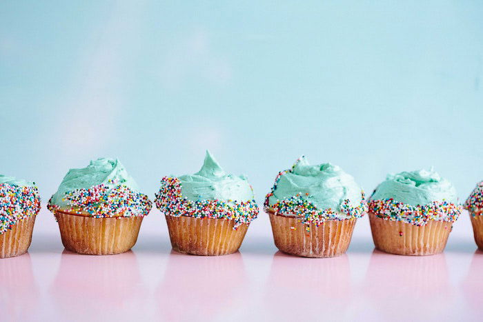 A group of six cupcakes with frosting and sprinkles. 