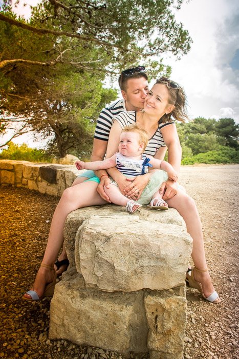 A couple and small child posing for a family portrait shoot by a stone wall