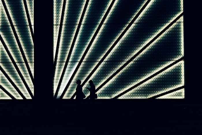 the silhouettes of people walking passed a lighted structure