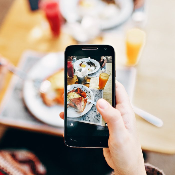 A hand holding a smartphone taking a picture of food and drink on a table as an example of food photography