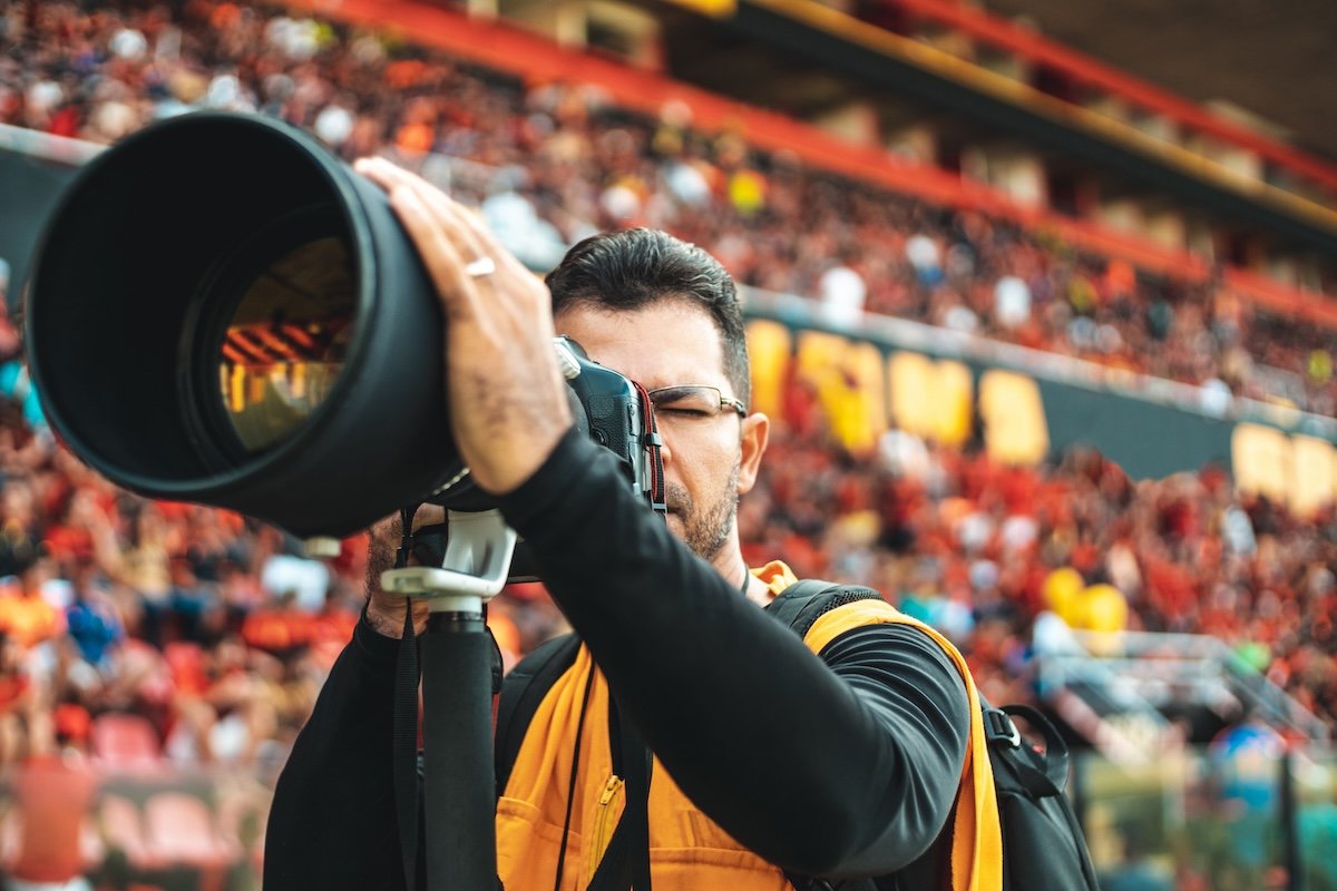 A sports photographer on the sidelines with a big super-telephoto lens