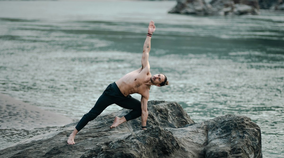 A man doing a yoga pose on rocks by the ocean as an example for sports photography