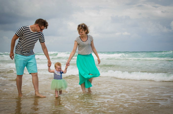 family of three walking through waves on a beach