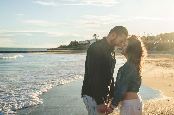 a couple close to each other holding hands on the shore with the beach and the sea around them