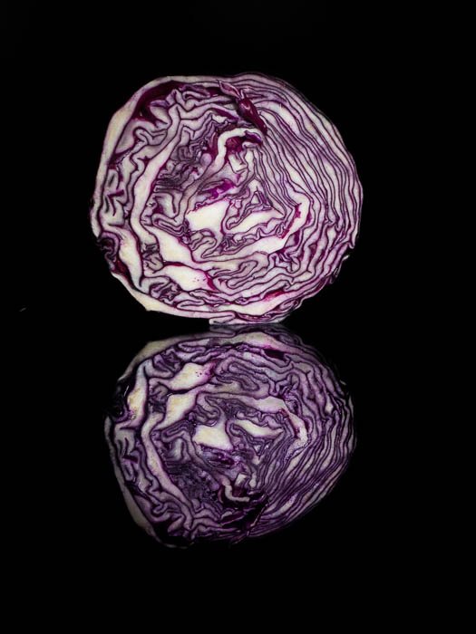 A half cabbage in front of a black background with its reflection
