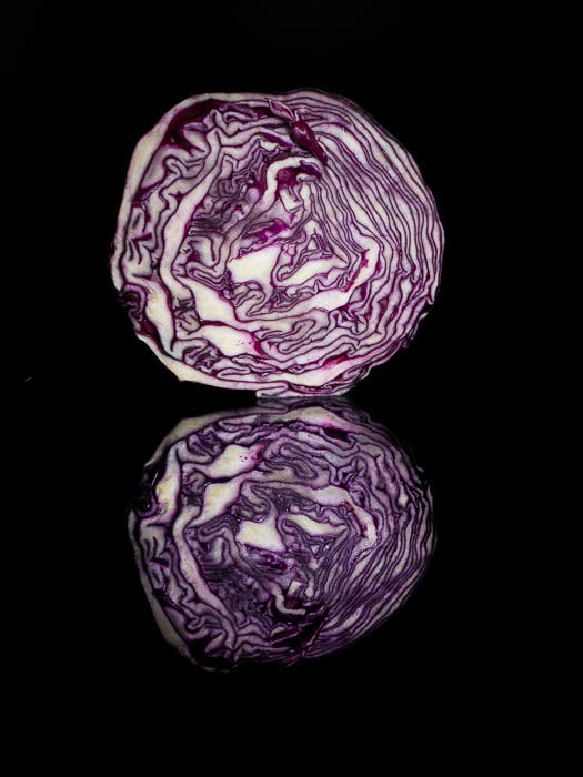 A half cabbage in front of a black background with its reflection