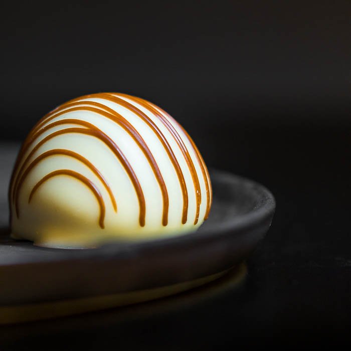 A closeup of a white praline on a grey plate in front of a black background