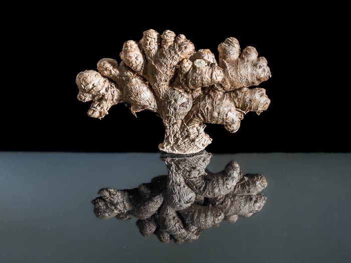 A ginger root in front of a black background with its reflection