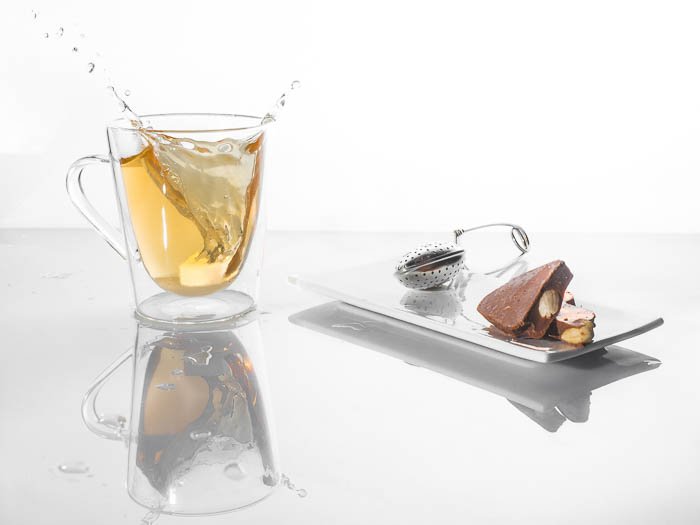 A minimalist food photo of a splashing cup of tea beside chocolates