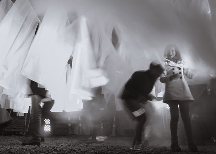 movement and blur in documentary photography - black and white photograph using slow shutter speed of people moving between white material 