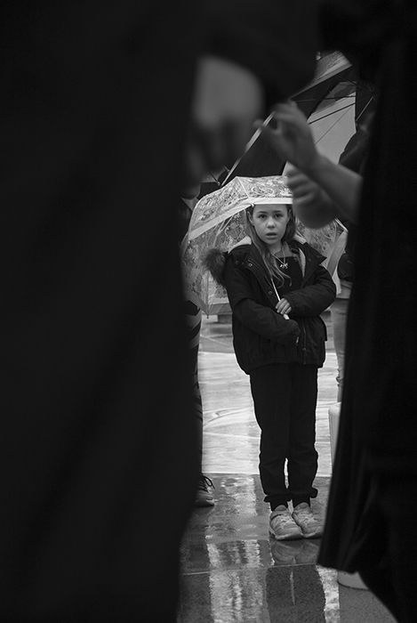 black and white documentary photography of a little girl holding an umbrella framed by larger figures