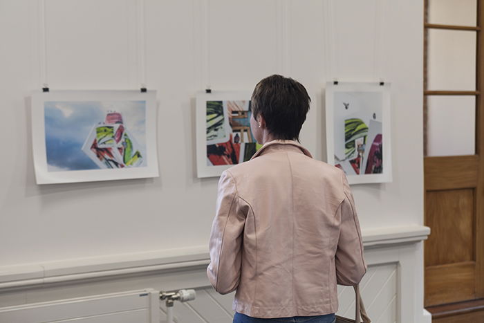 woman in pink jacket looking at paintings in an art exhibition