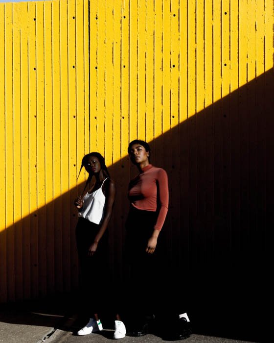 Two female model posing outdoors against a yellow wall - fashion photography composition