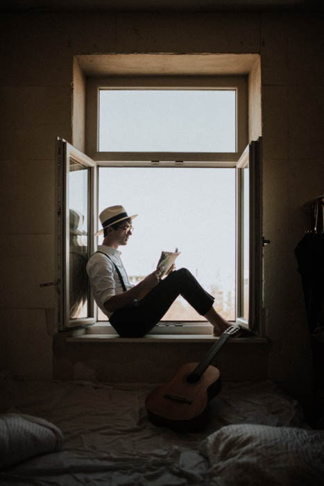 A man sitting in a window frame reading