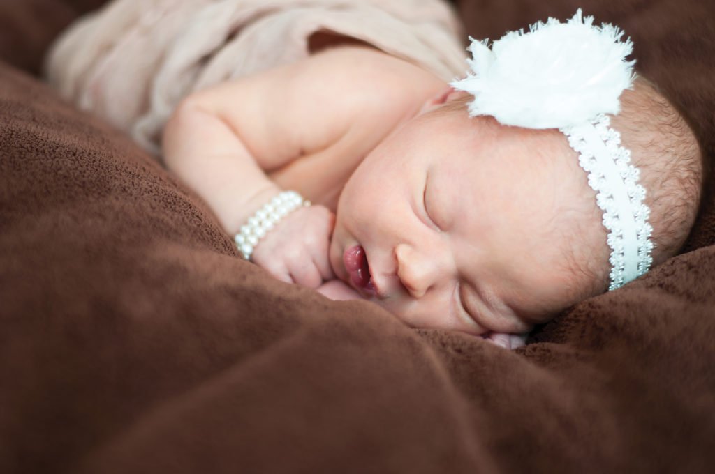 close up portrait of a newborn baby on brown material, wearing a pearl headband and bracelet. newborn photography