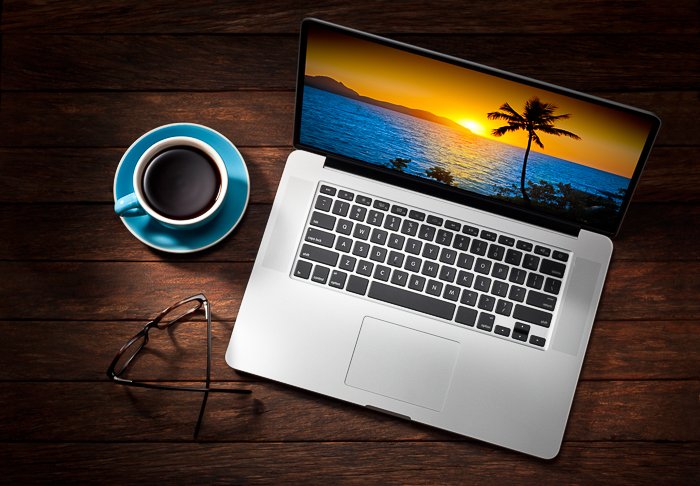 a laptop with sunset screensaver, glasses and coffee cup on a wooden table.