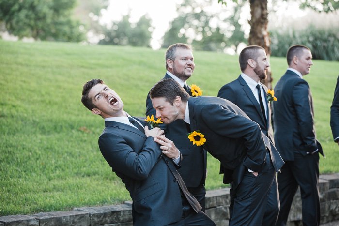 A humourous wedding photo depicting a group of groomsmen, one smelling the sunflower in another mans lapel
