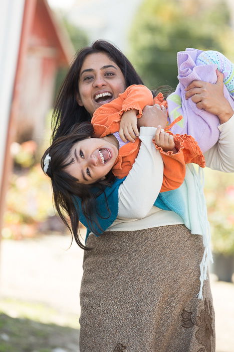 Outdoor portrait of a mother holding her daughter playfully upside down, both smiling towards the camera