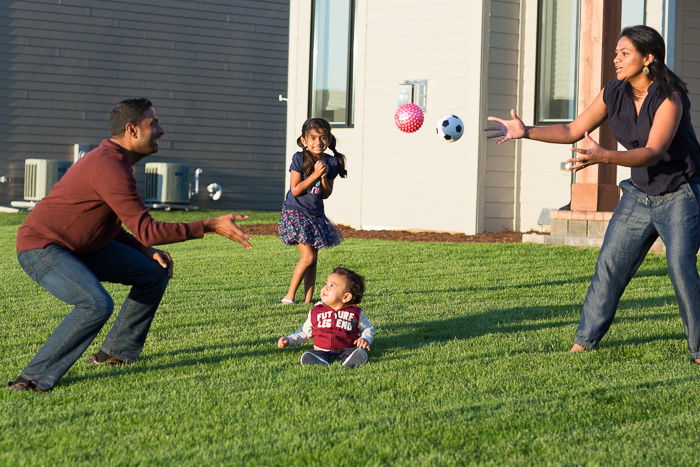 candid portrait of a father and mother playing catch with two young children in the garden