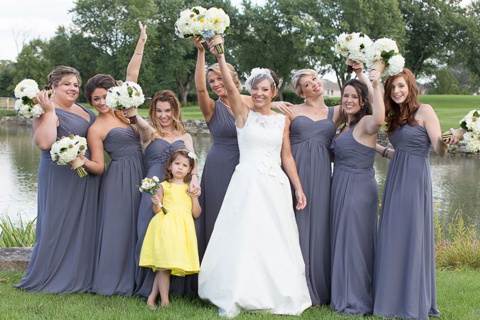 Playful wedding lifestyle shot showing the bride with 7 bridesmaids and 1 flower girl holding bouquets of white flowers in the air